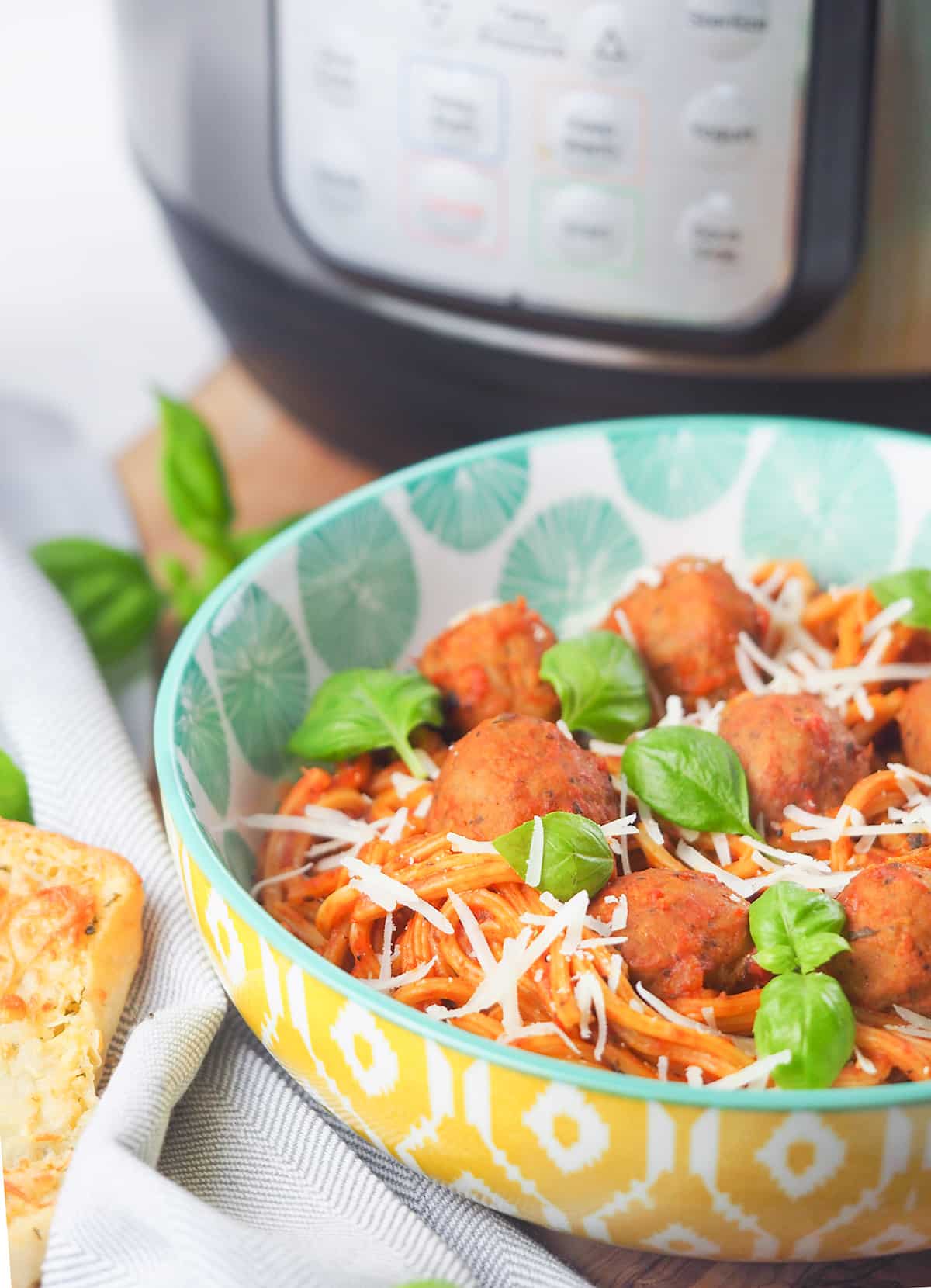 spaghetti in bowl topped with basil and parmesan cheese in front of Instant Pot