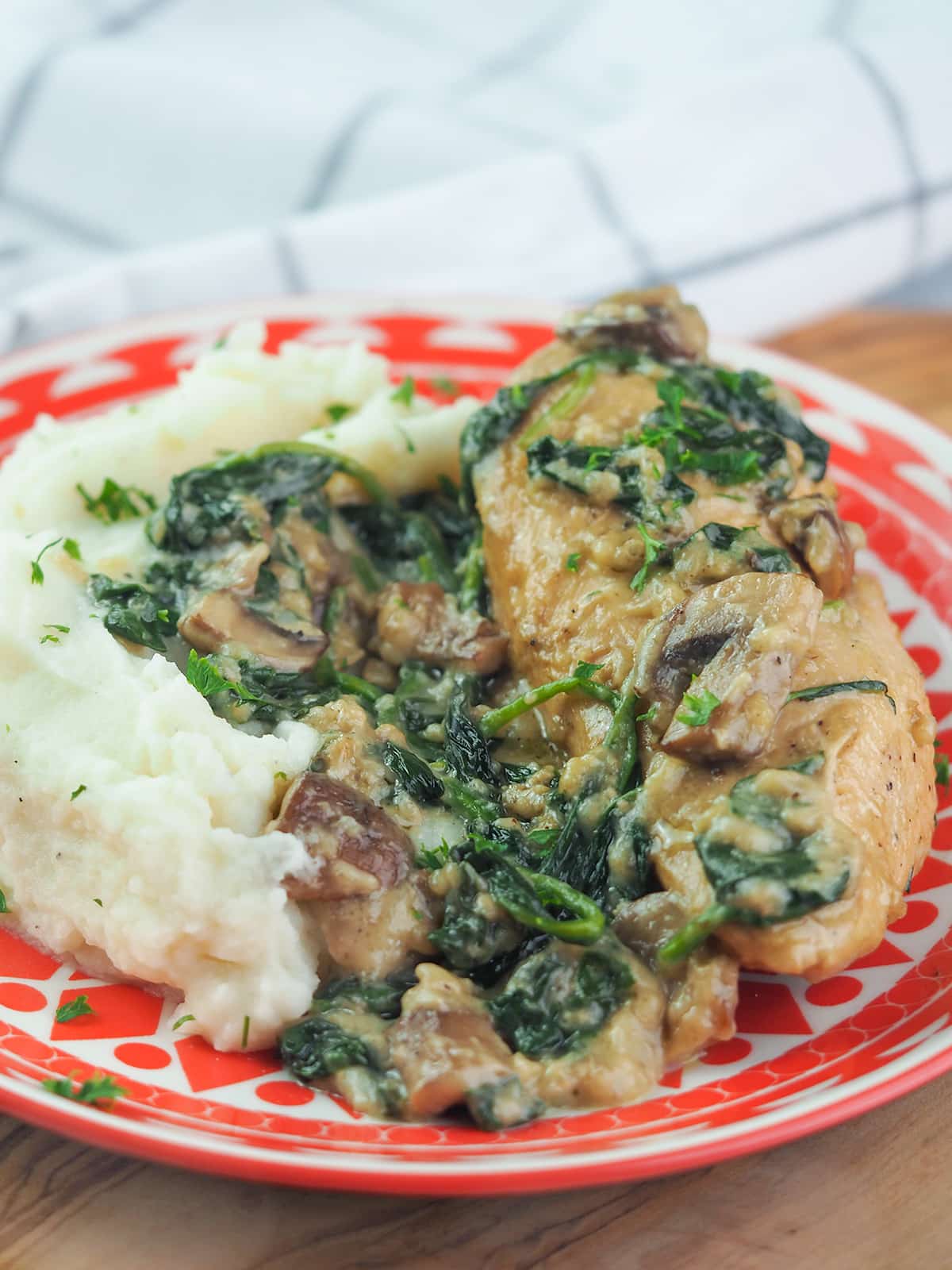 chicken and mushrooms on red plate topped with spinach and next to potatoes