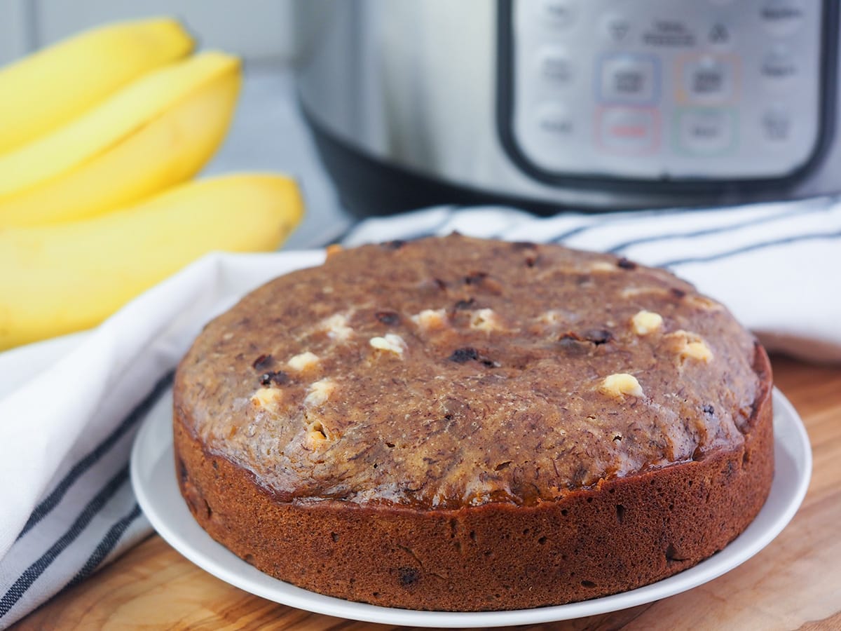 loaf of banana bread on plate in front of Instant Pot and fresh bananas