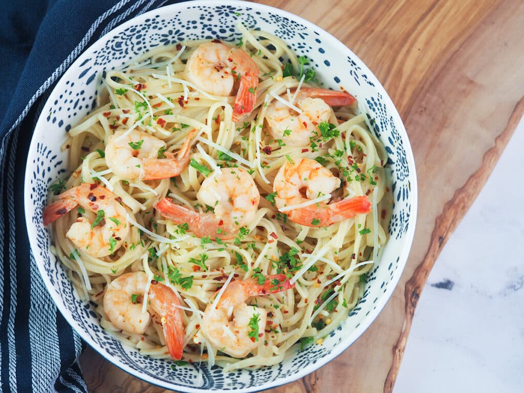 shrimp scampi pasta in blue and white bowl on cutting board