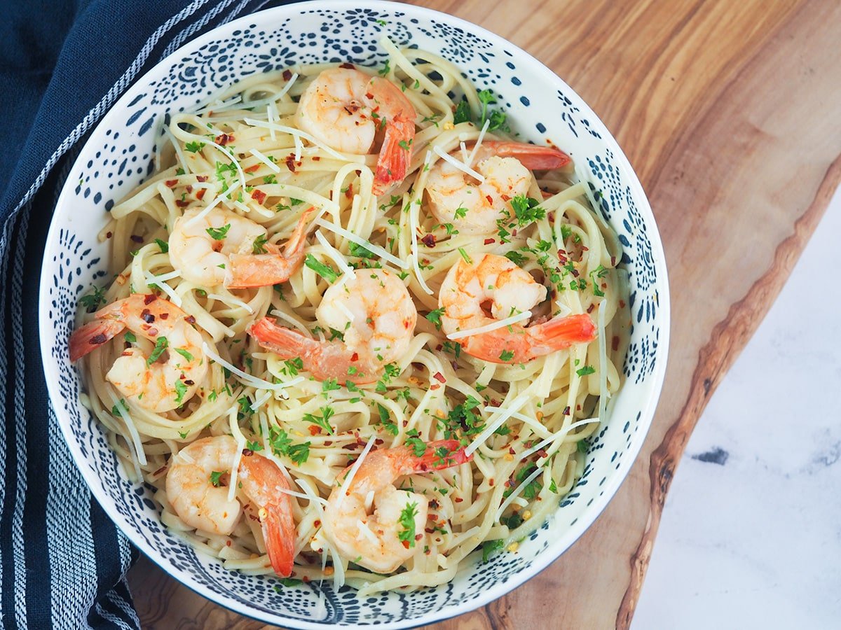 shrimp scampi pasta in blue and white bowl on cutting board