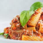 close view of bolognese sauce and pasta topped with basil and parmesan cheese