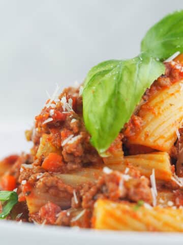close view of bolognese sauce and pasta topped with basil and parmesan cheese