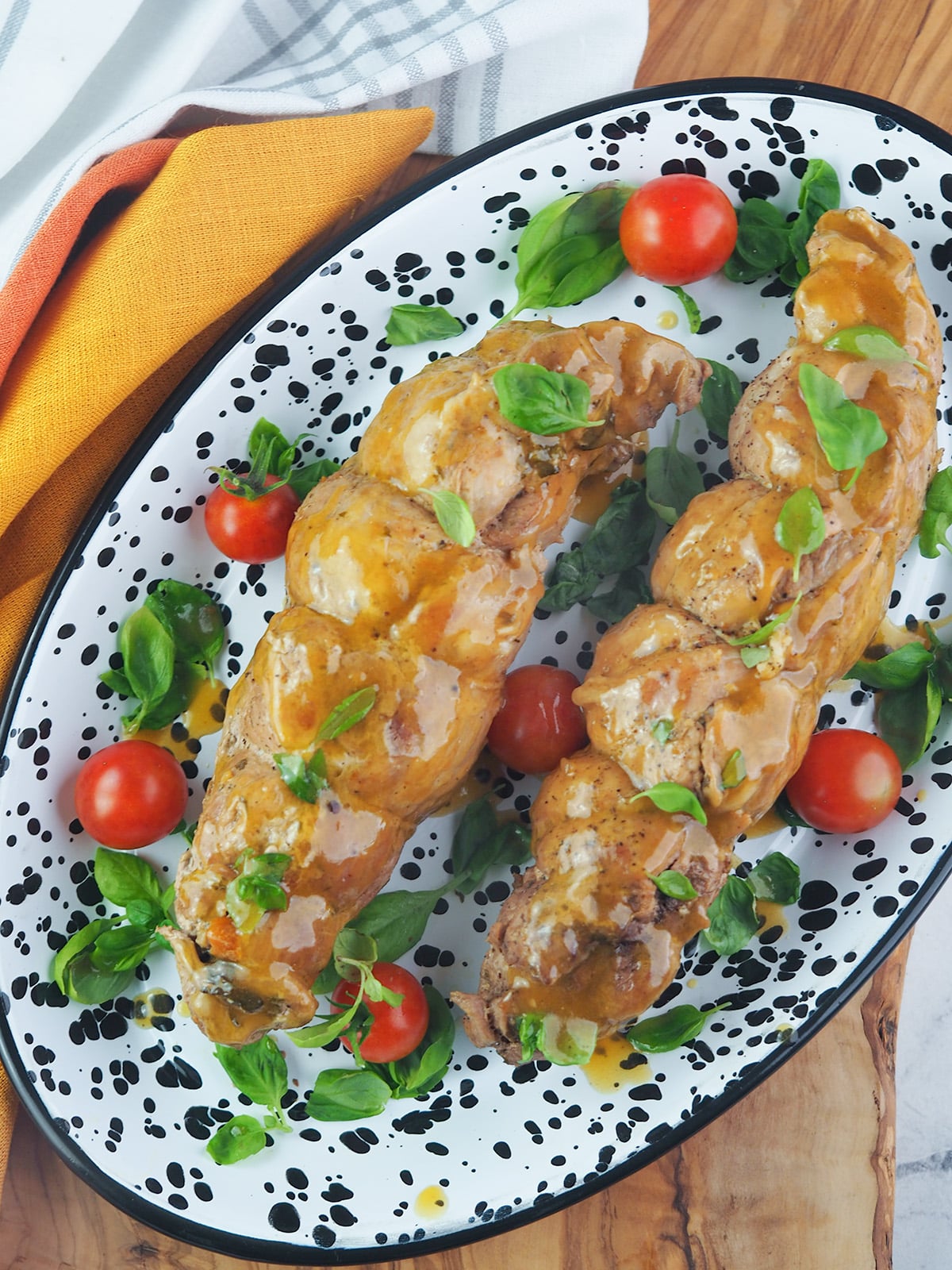 Two pork tenderloins on black and white enamelware with fresh cherry tomatoes and basil.