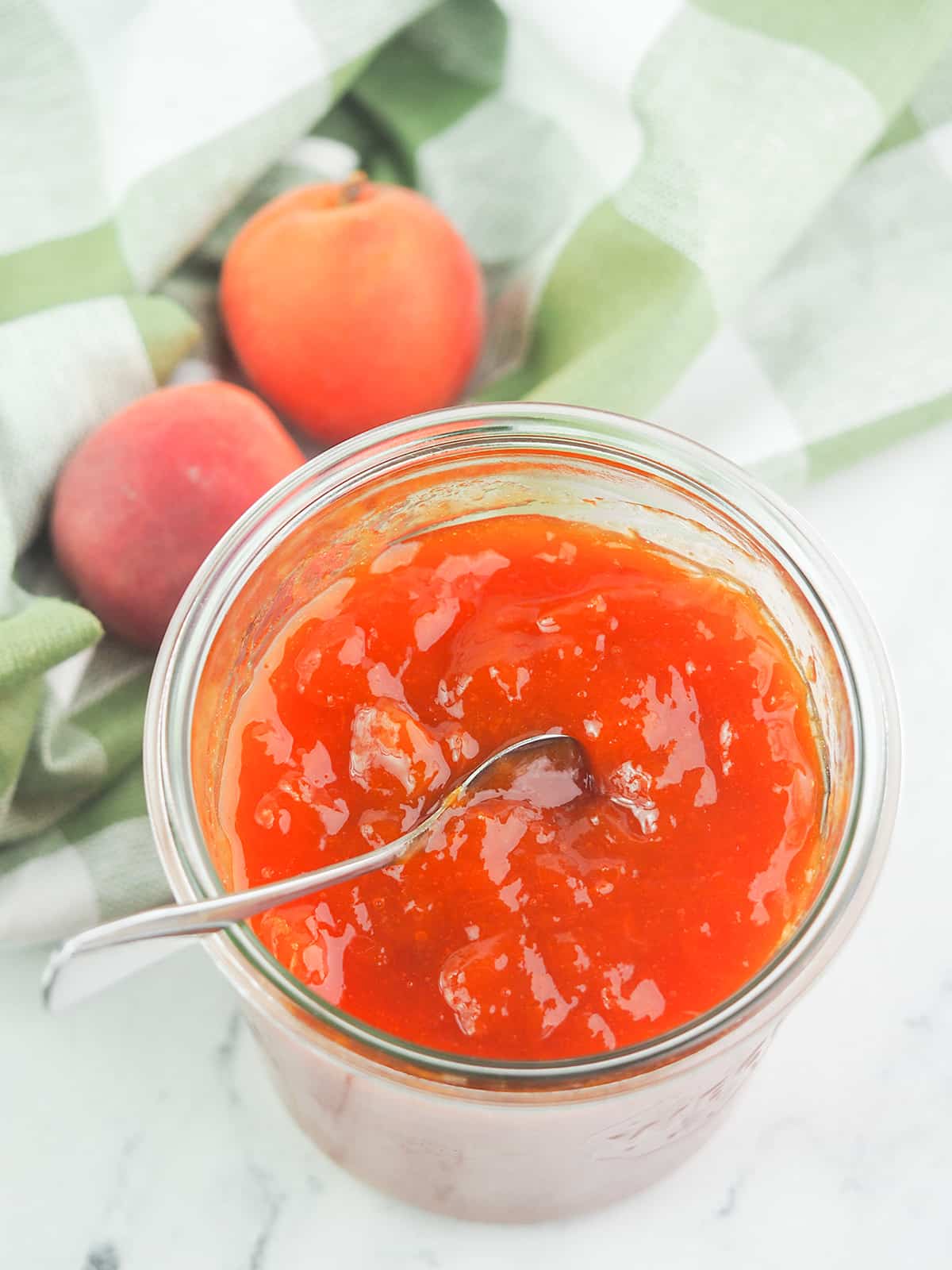 apricot jam with spoon in jar next to green linens