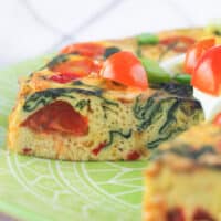 frittata on green plate with a slice removed topped with tomatoes and sour cream