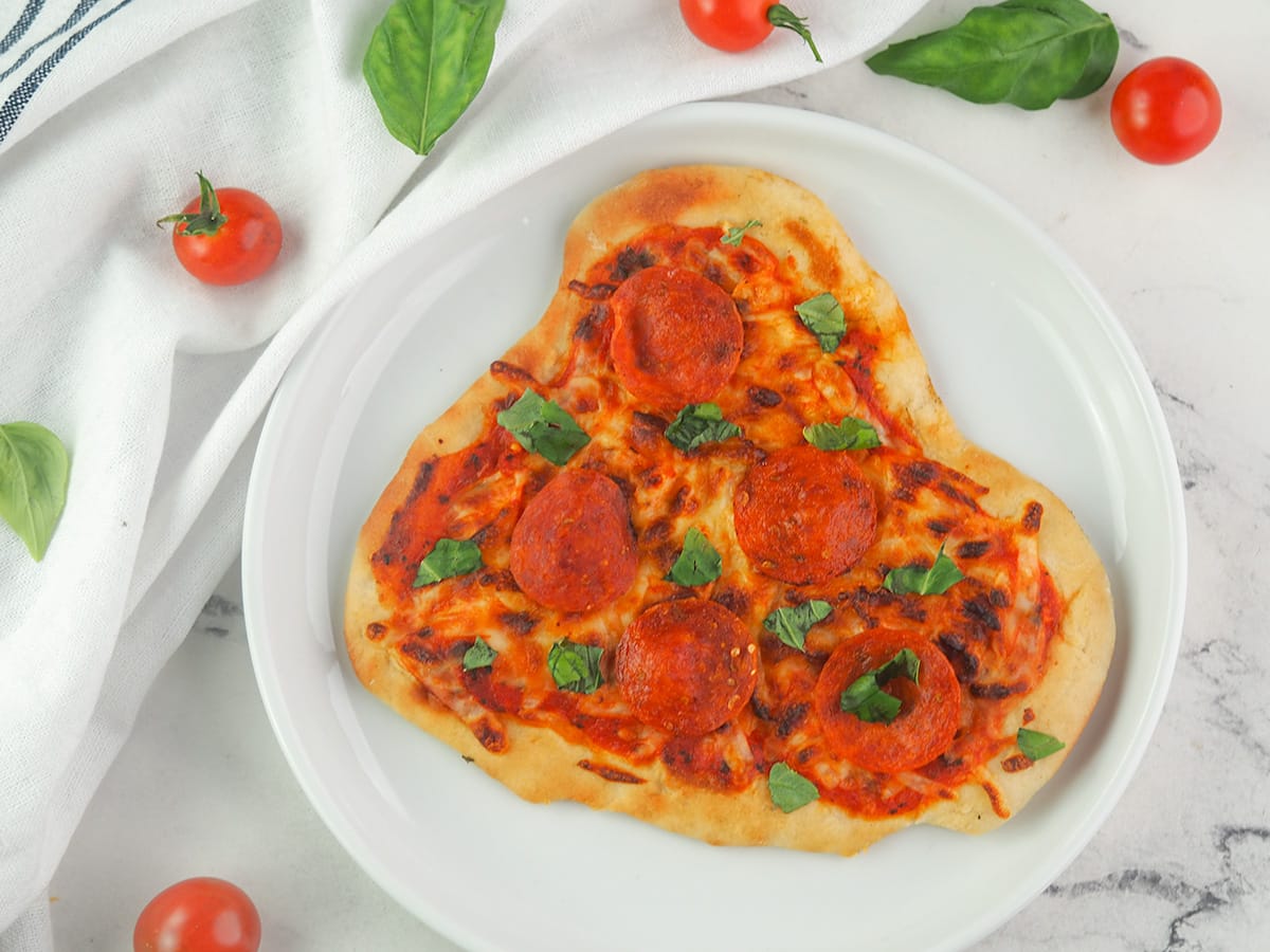naan pizza on white plate with basil and tomatoes