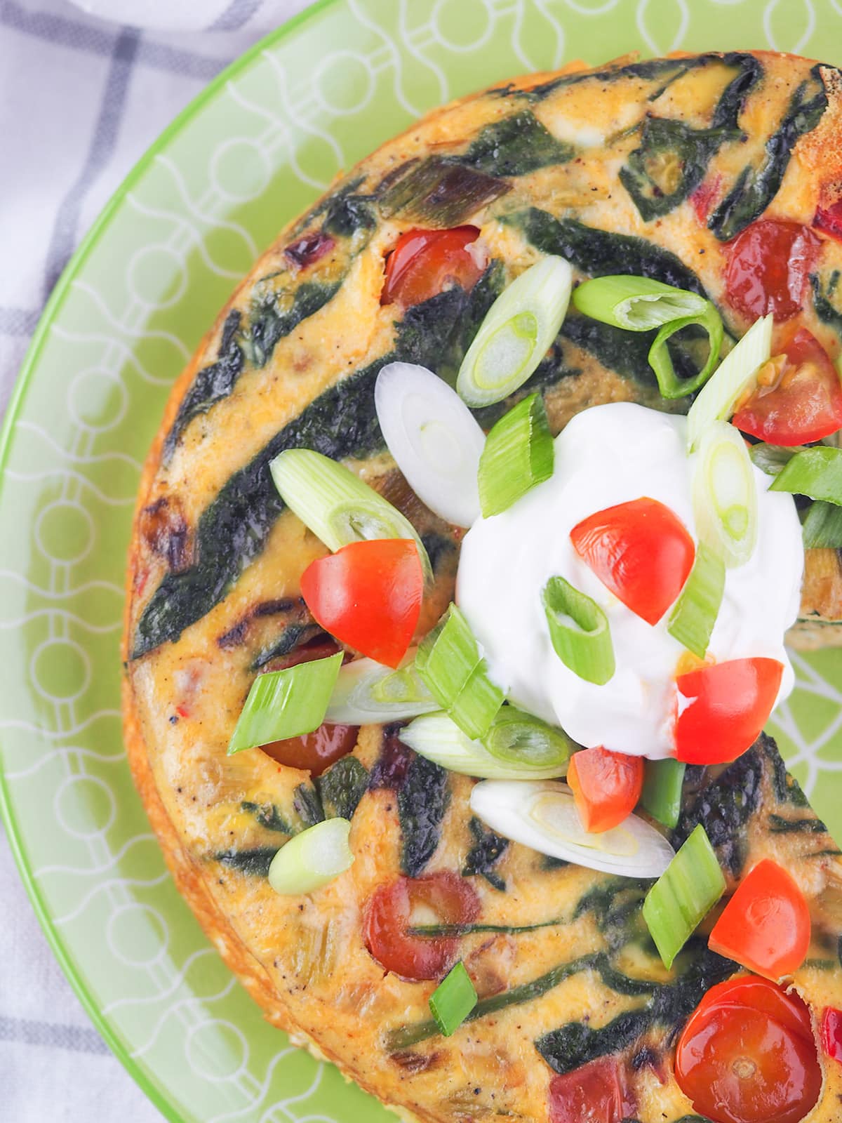 whole frittata on green plate topped with green onoins, tomatoes, and sour cream