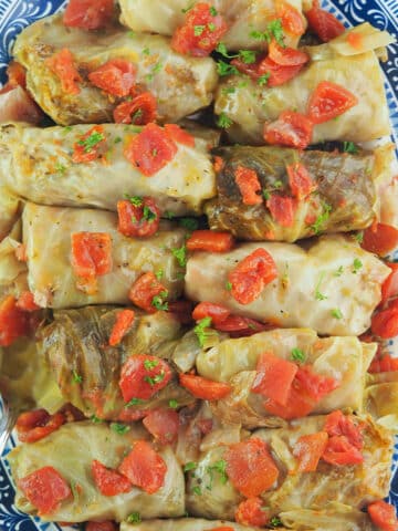 cabbage rolls on blue and white platter topped with diced tomatoes
