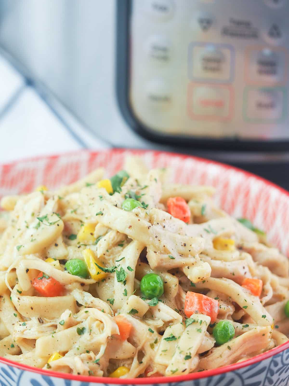 chicken noodles with vegetables in bowl in front of instant pot