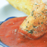 Breadstick being dipped in marinara sauce.