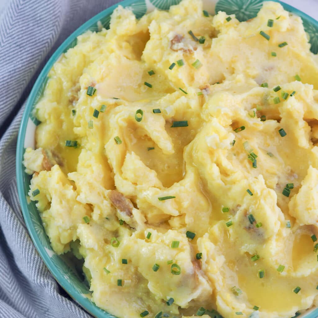 Close view of buttered garlic mashed potatoes in aqua bowl topped with chives.