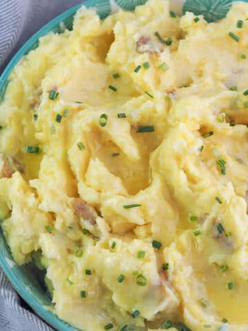 Close view of buttered garlic mashed potatoes in aqua bowl topped with chives.