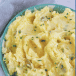 Mashed potatoes in aqua bowl topped with butter and chives.