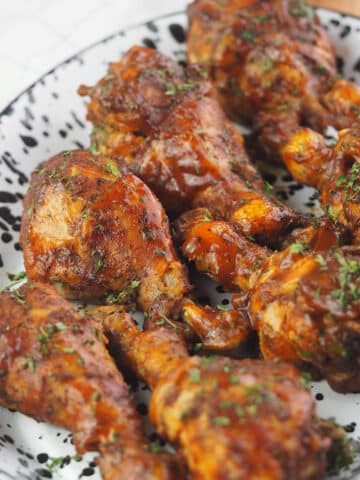 BBQ chicken legs on black and white enamelware platter sprinkled with parsley.