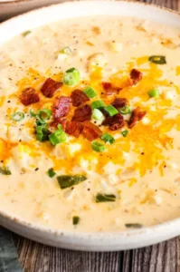 Cauliflower on table in stoneware bowl topped with bacon, green onions, and cheese.