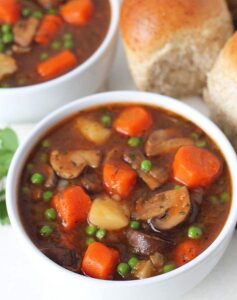 Mushroom stew with carrots and peas on small white bowl.
