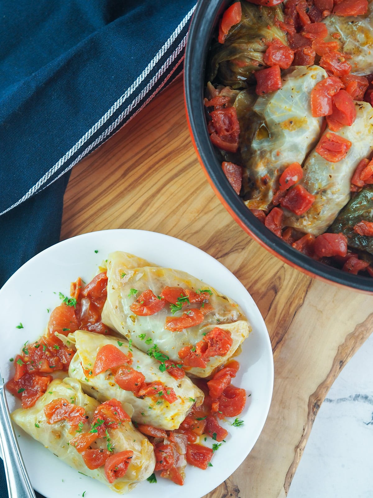 cabbage rolls on cutting board next to dutch oven filled with cabbage rolls
