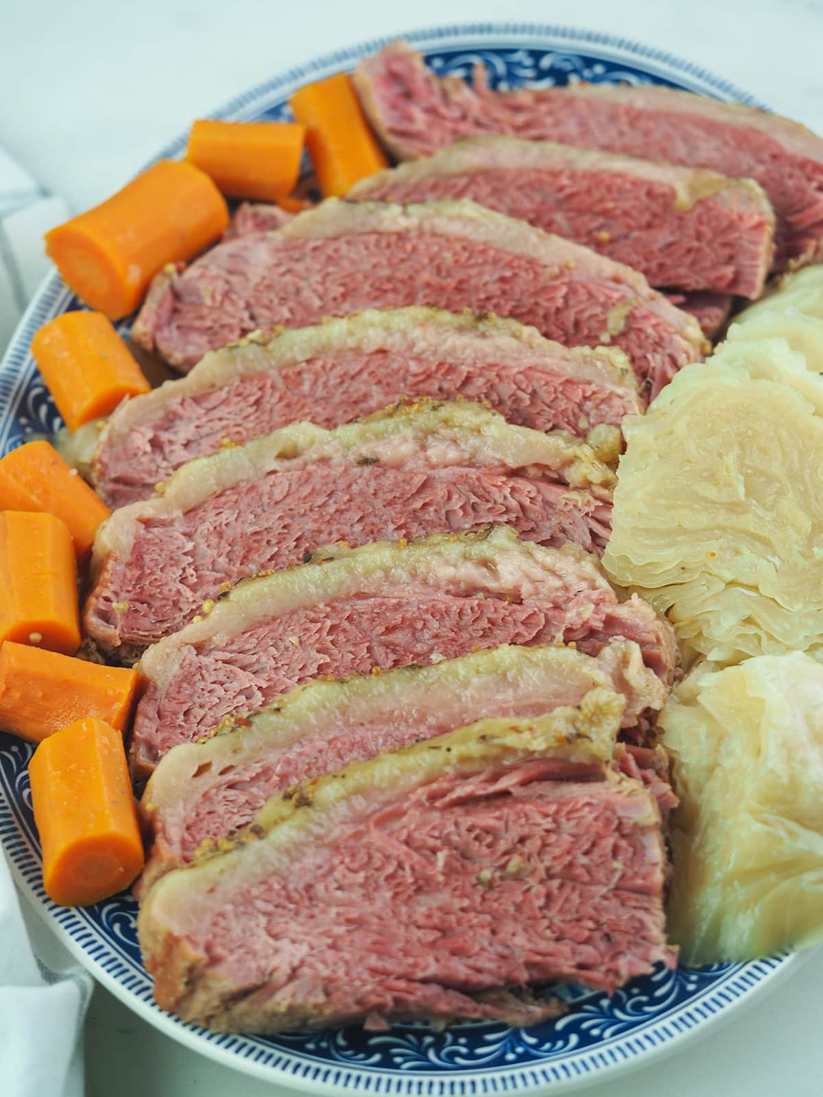 sliced corned beef on blue and white platter with cabbage and carrots