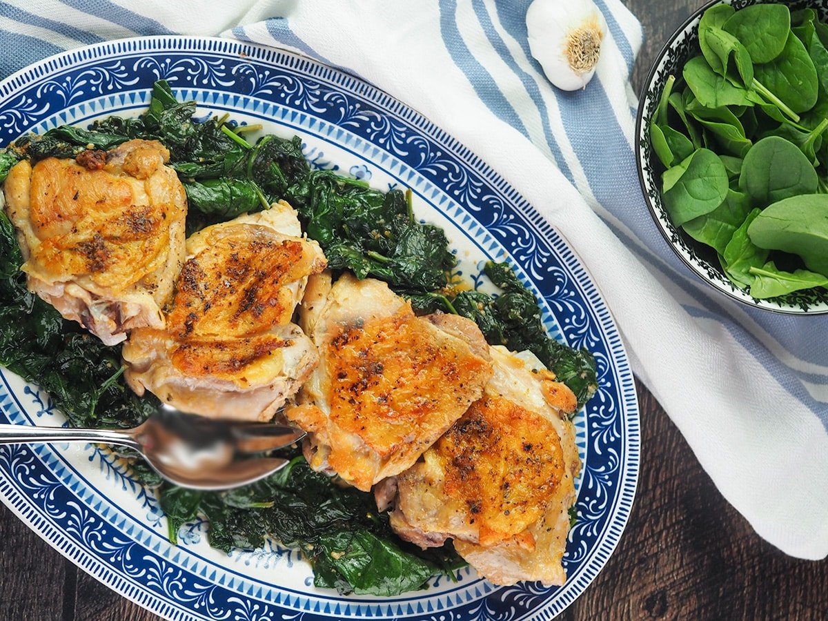 horizontal chicken thighs on blue platter resting on bed of spinach