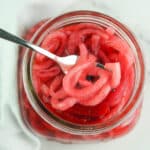 Overhead of pickled red onions in mason jar with fork picking some up.